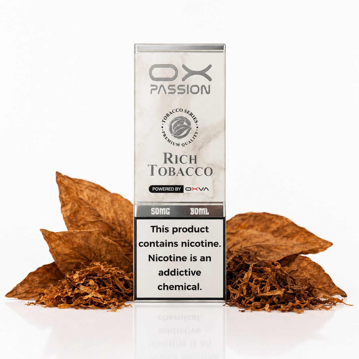 A box of OX Passion Rich Tobacco e-liquid stands upright on a white reflective surface, surrounded by scattered brown tobacco leaves and shreds. The packaging is white and gray with black text, and a nicotine warning label is visible on the lower front.